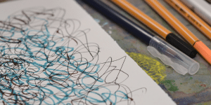 Close up of paper covered in blue and black squiggles and pencils.