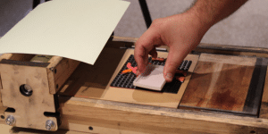 Hand stamping a Lego design on a handmade printing press.