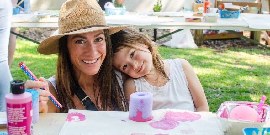 Mother and young daughter smiling together at a arts and craft table =.