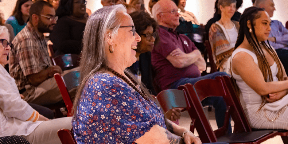 Older woman in focus smiling in a group of people listening to a talk.