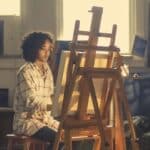 a young african american woman works at an easel on a canvas