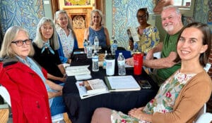 group of diverse people at a table in a room where the walls are covered with complex murals