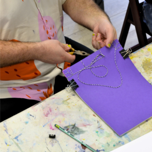 A man book binds using the Japanese method pulling twine through the stack of papers.