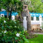 A beautiful garden with an ornate sculpted gate topped with an antique bell