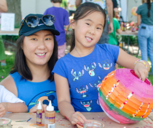 A mother and daughter smile at the camera holding a colorful paper lantern.