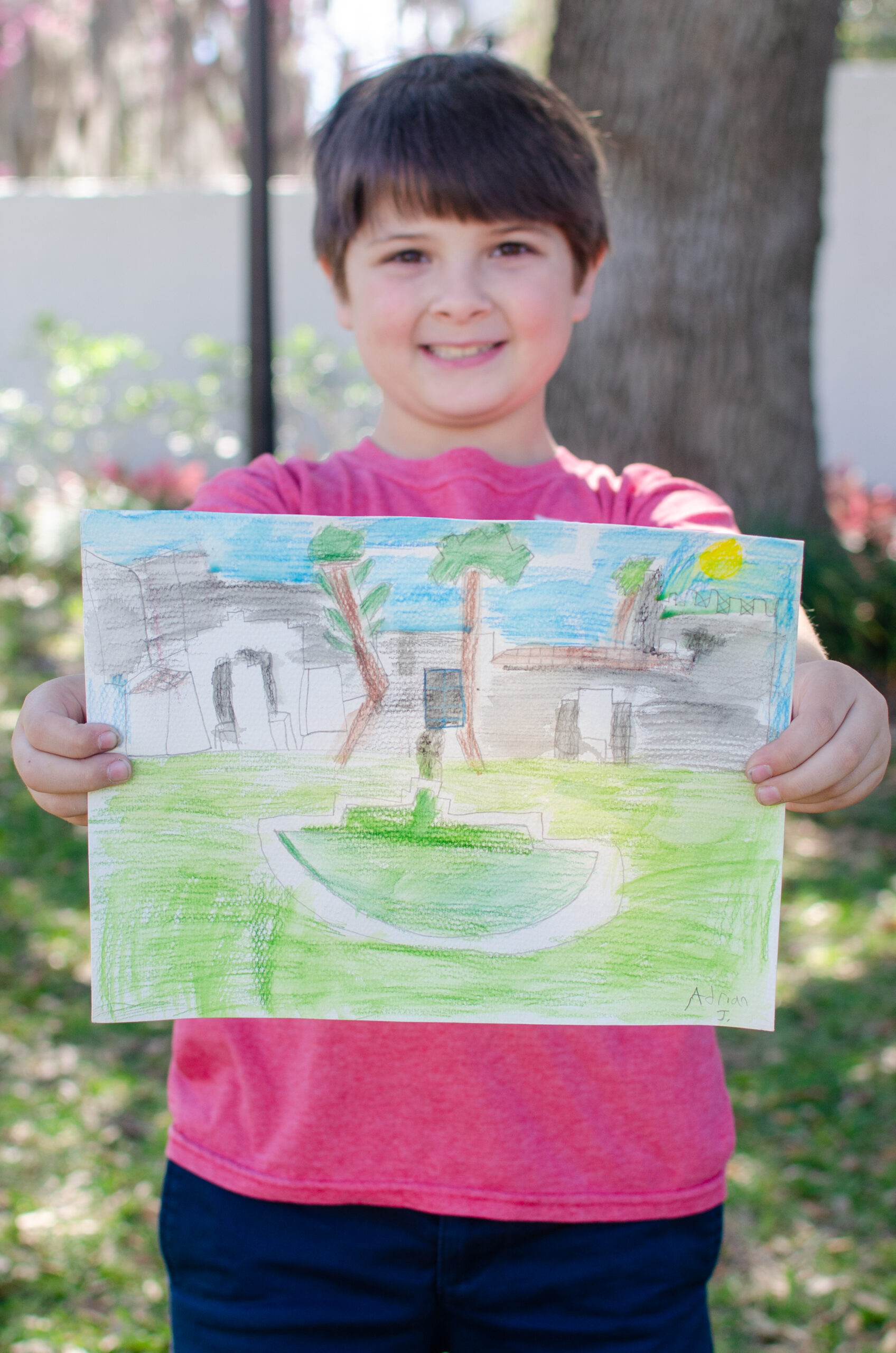 A young boy smiling and holding out his drawing of the museum.