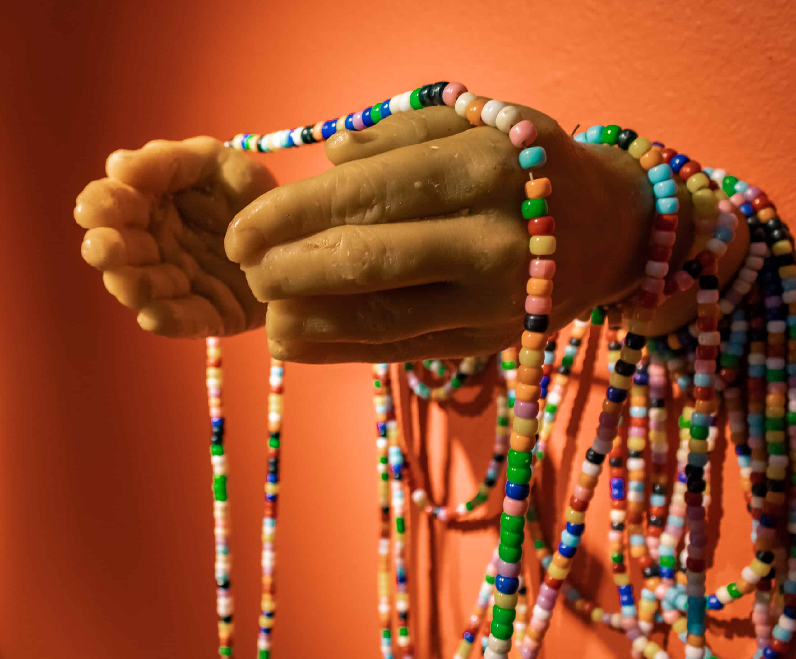 The artists' hands cast in tan wax and wrapped in draping strings of colorful pony beads