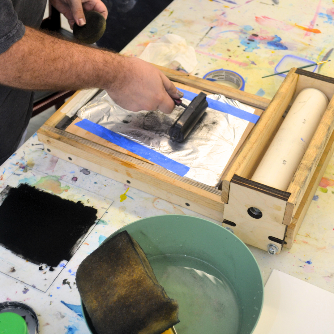 A man rolls ink onto a kitchen litho making a print of his image.