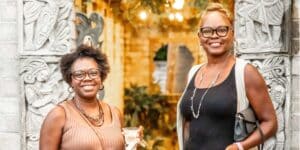 Two women standing next to each other posing in front of the A&H Mayan Courtyard Gates.