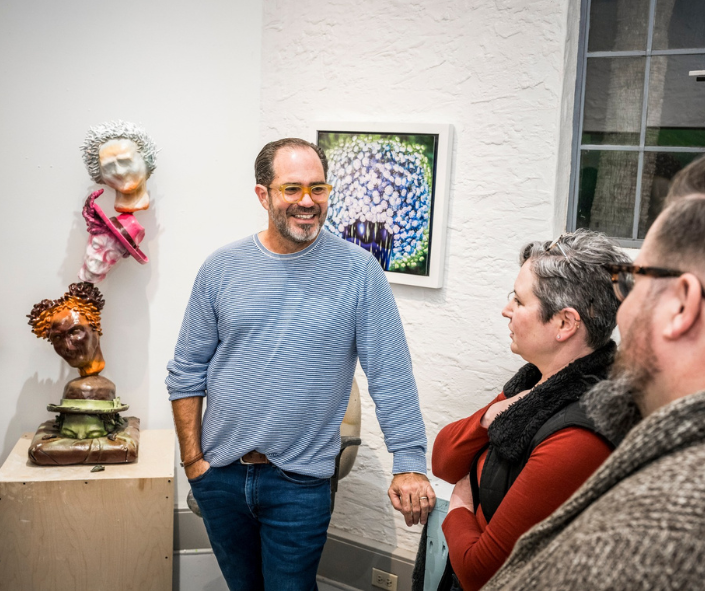 Artist smiling in an art studio at a couple having a discussion.