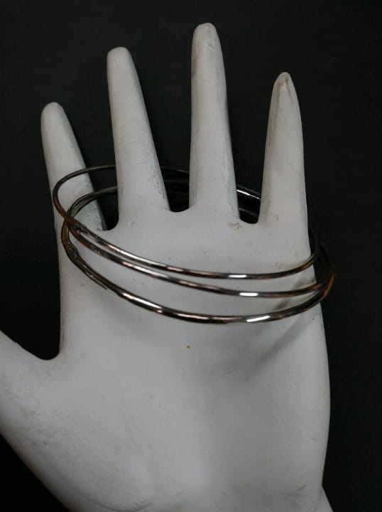 A set of three handmade silver bracelets rests atop a hand-shaped display stand.