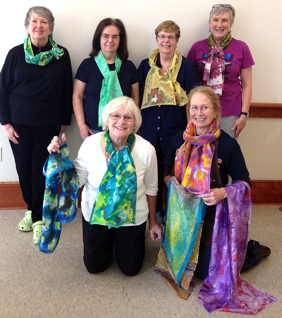 A group of light-skinned women, middle to senior aged, modeling their colorful hand painted silk scarves with smiles
