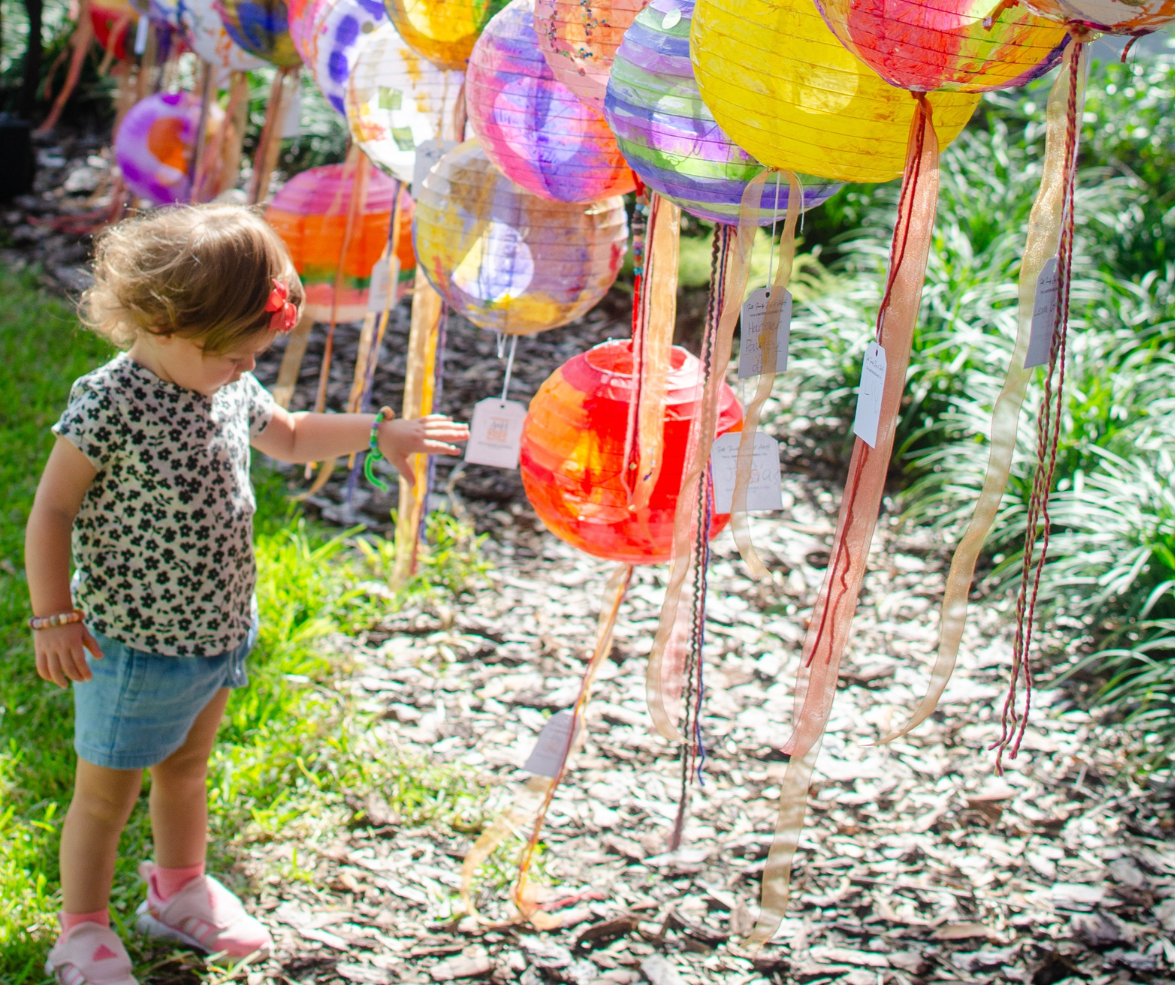 A young girl looking down inquisitively at a row of colorful hanging paper lanterns in the Main Garden.