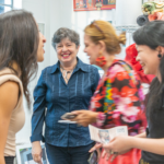 A photo of a woman smiling in the background while other people happily mingle in the foreground and middle ground.
