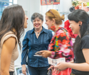 A photo of a woman smiling in the background while other people happily mingle in the foreground and middle ground.