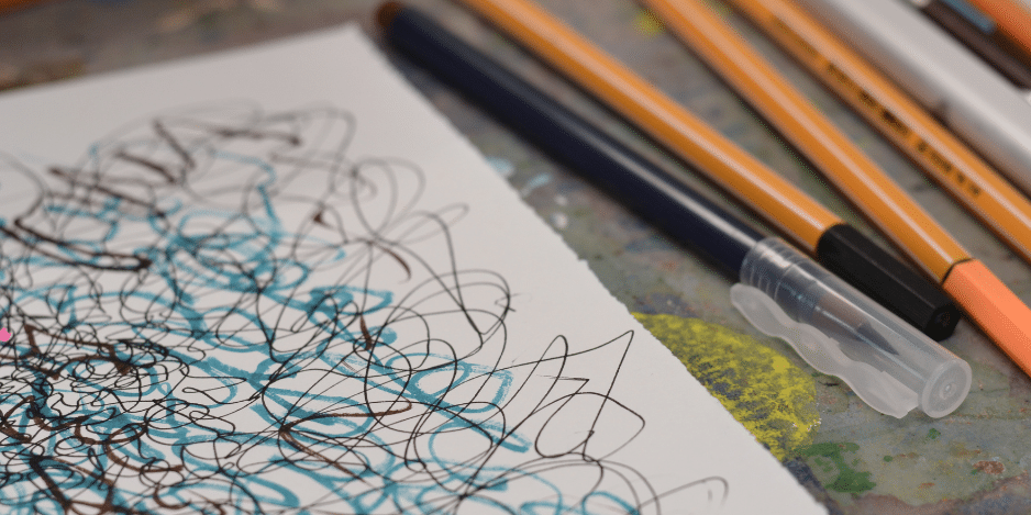 Close up of paper covered in blue and black squiggles and pencils.