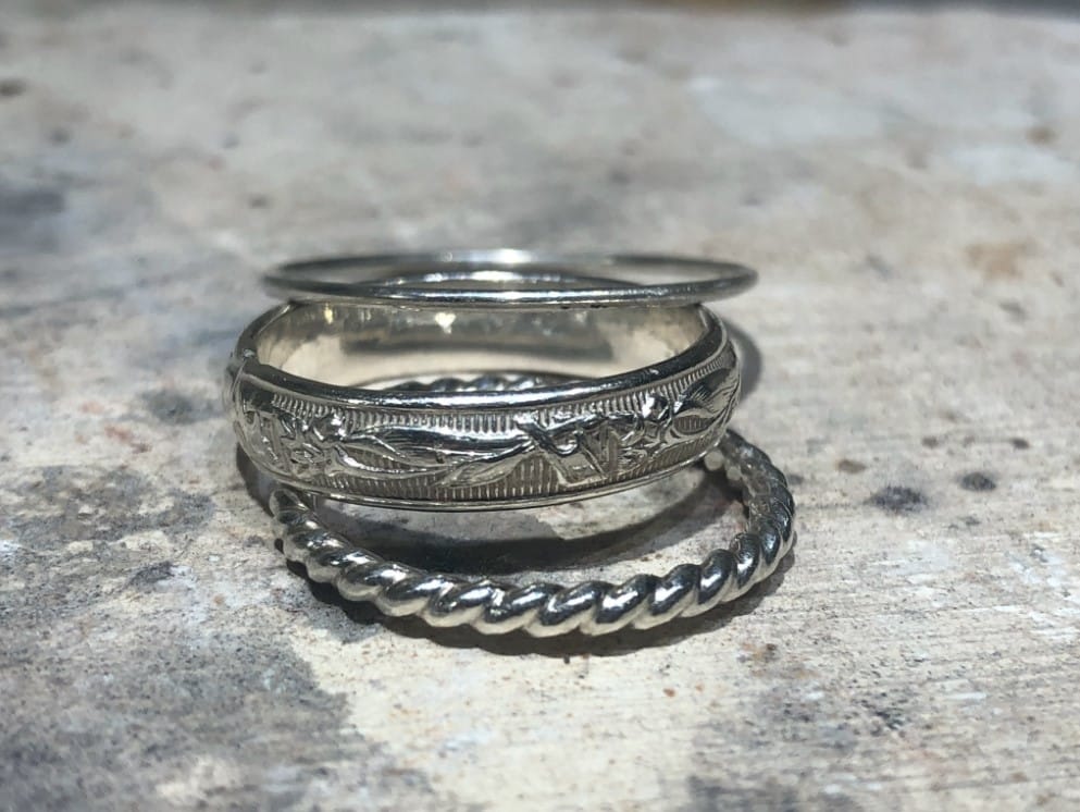 A set of three handmade silver rings sitting atop a marbled surface.